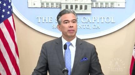 A man in a suit speaks at a podium with microphones in front of him. Behind him is a circular emblem with text stating "THE CAPITOL SACRAMENTO, CA." American flags are visible on either side of him as he discusses California's marijuana reform from 2018. CA Norml