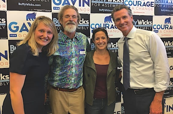 Four individuals standing in front of a backdrop with campaign signs promote Gavin for Governor and Buffy Wicks. The two women are smiling on both ends, one man with a beard and glasses is in the middle-left, and another man in a tie is on the middle-right. These California candidates proudly support pro-cannabis legislation. CA Norml