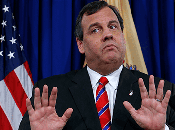 A man in a dark suit and red-striped tie stands in front of American and yellow flags. With hands raised, palms outward, and a serious expression on his face, he addresses the Opioid Commission. Blue curtains are visible in the background. CA Norml