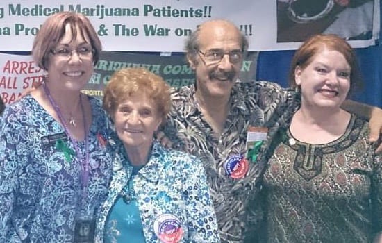 Four people are standing close together, smiling at a camera. Behind them is a banner with text that is partially visible, referencing medical marijuana patients. They appear to be at an event or gathering supporting Democrats' platform on marijuana legalization. CA Norml