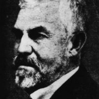 Black and white side profile portrait of an older man with short, white hair and a full beard and mustache. The man is wearing a dark suit and a bow tie. The background is dark, emphasizing his facial features and formal attire, reminiscent of California's dignitaries who saw the 100-year-old ban on marijuana. CA Norml