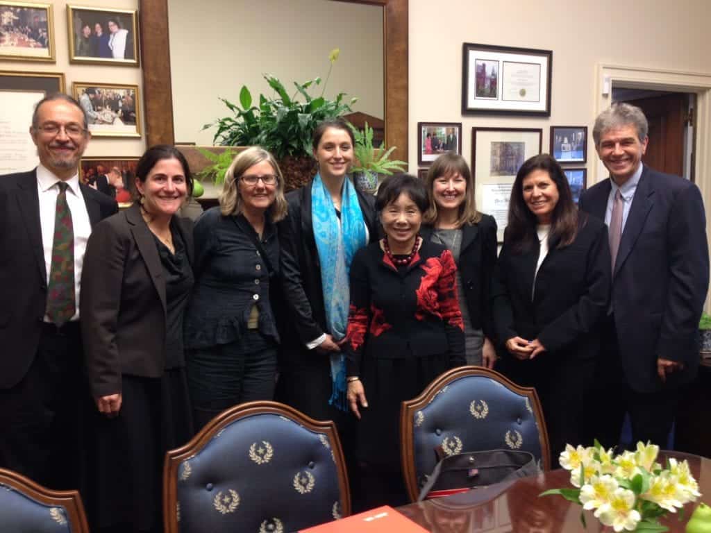 A group of eight reformers, dressed in formal business attire, stand in an office setting on Capitol Hill, smiling at the camera. The room has framed certificates and photographs on the walls, a green plant on a wooden cabinet, and a table with floral arrangements in the foreground. CA Norml