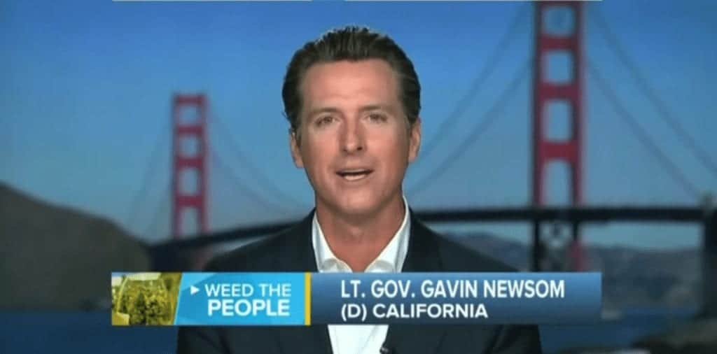 A man in a suit and white shirt speaks in front of an image of the Golden Gate Bridge. The text on the screen reads, "WEED THE PEOPLE" and "LT. GOV. GAVIN NEWSOM (D) CALIFORNIA." Amid growing concerns over Jeff Sessions' stance on marijuana prosecution, Newsom advocates for California's cannabis laws. CA Norml