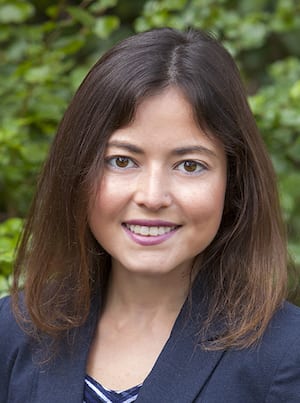 A woman with shoulder-length brown hair and brown eyes smiles at the camera. She is wearing a navy blue blazer over a blue and white striped top, likely at the 2021 Legal Seminar hosted by California NORML, with a blurred background of greenery. CA Norml