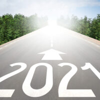 A straight road stretches into a bright light, with "2021" and a forward-pointing arrow painted on it. On the right, a yellow road sign with the word "ADVOCACY" stands near dense green foliage under a partly cloudy California sky. CA Norml