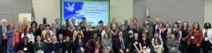 A large, diverse group of people posing for a photo in a conference room. A presentation screen behind them reads "California Citizen Lobby Day: Equal Rights, Fair Taxation, Sensible Regulation, May 4, 2023, Sacramento, CA." Everyone is smiling and celebrating the event and their 2023 accomplishments with Cal NORML. CA Norml