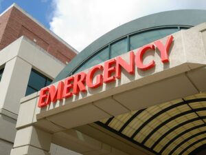 Entrance to an emergency room at a hospital, marked by a prominent red "EMERGENCY" sign above a covered walkway, set against a backdrop of a light-colored building and partly cloudy sky. This California facility is equipped to handle various situations, including RAP-C incidents and cannabis overdoses. CA Norml