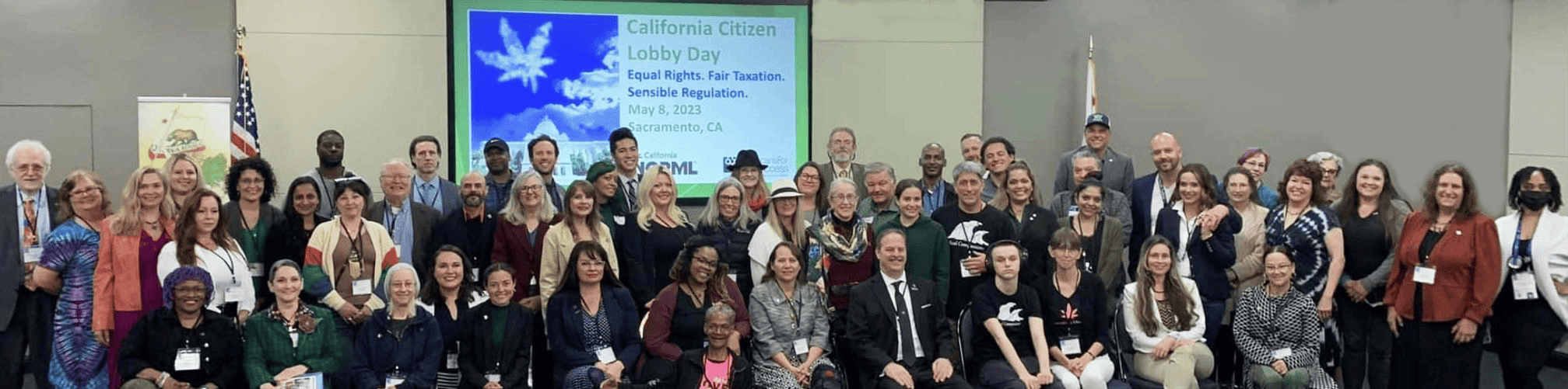 A large, diverse group of people is posing for a group photo in front of a screen displaying "Citizen Lobby Day in Sacramento 5/8/2023." The slide mentions "Equal Rights, Fair Elections, Sensible Regulation" and notes the event date as May 10, 2023, in Sacramento, CA. CA Norml