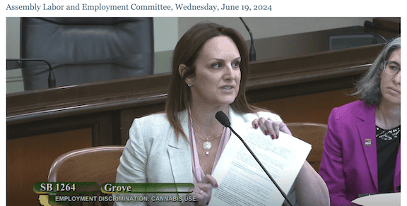 A woman in a light-colored blazer speaks while holding papers at an Assembly Labor and Employment Committee meeting on Wednesday, June 19, 2024. The text at the bottom of the screen reads "SB 1264" and "Grove," highlighting discussions about employment protections related to off-the-job cannabis use. CA Norml