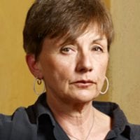 A woman with short brown hair and wearing a black shirt is looking at the camera with a neutral expression. She is wearing hoop earrings and a silver necklace with a circular pendant, embodying both style and the cause of racial justice. The background is softly lit in earthy tones. CA Norml