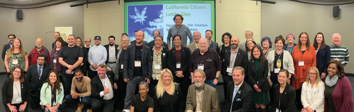 A group of around 40 people pose together in a conference room. They are gathered in front of a screen displaying "California Citizen Lobby Day," with a subtitle about equality and fairness. Most are smiling, some wear name tags, and the mood appears positive and collaborative as they discuss 2022 accomplishments and plans for 2023 with Cal NORML. CA Norml