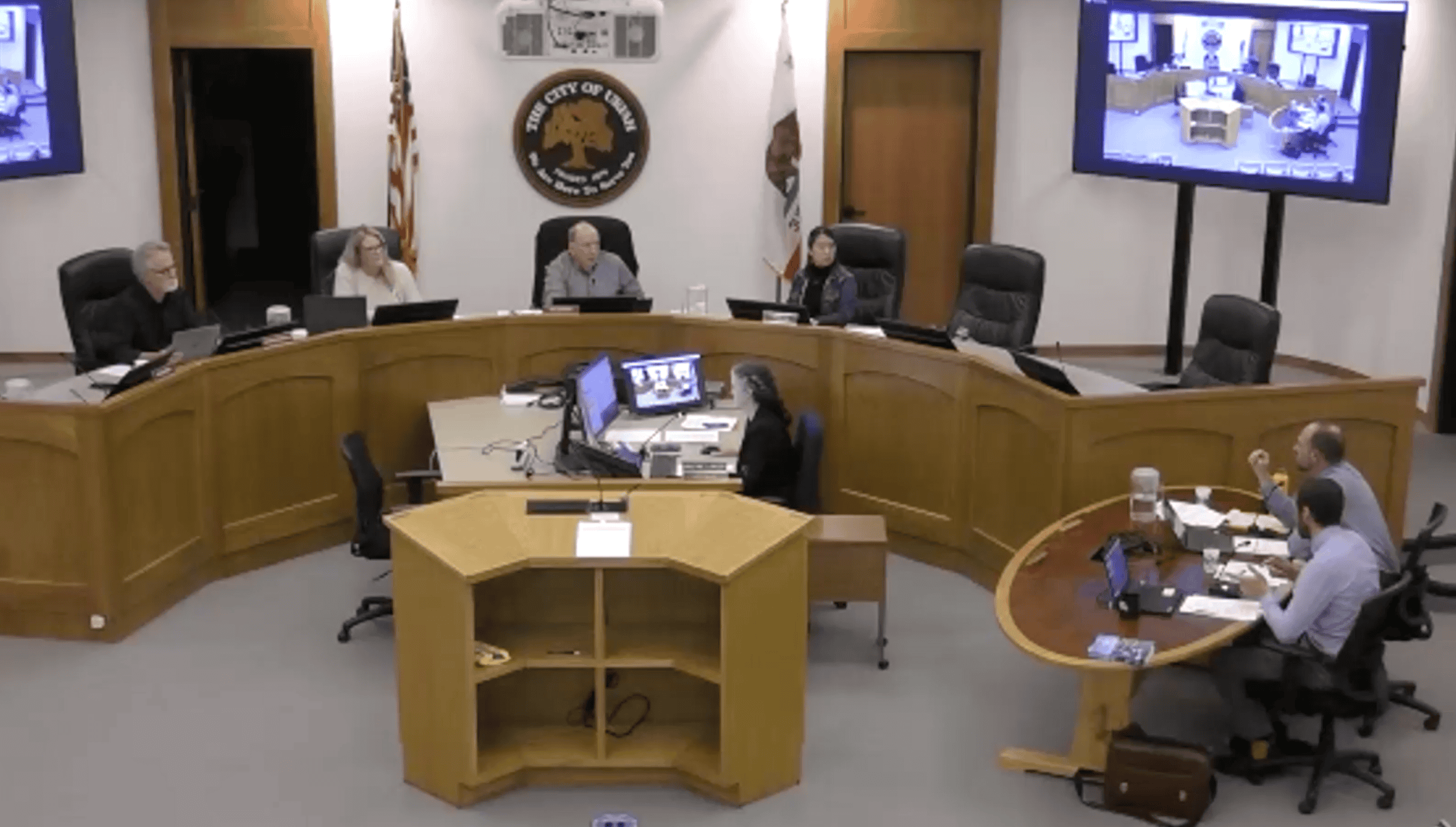 A Ukiah Planning Commission meeting setup is shown with four officials seated at a curved desk facing a large wooden podium. Three additional people are seated at a round table to the right. A large screen above shows a video call discussing the new cannabis consumption ordinance. CA Norml