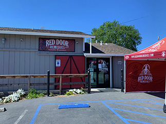 A gray building with a red sign reading "Red Door Remedies" above the entrance. A red tent featuring the Red Door Remedies logo is set up outside, and a wheelchair-accessible parking spot is visible in front. CA Norml
