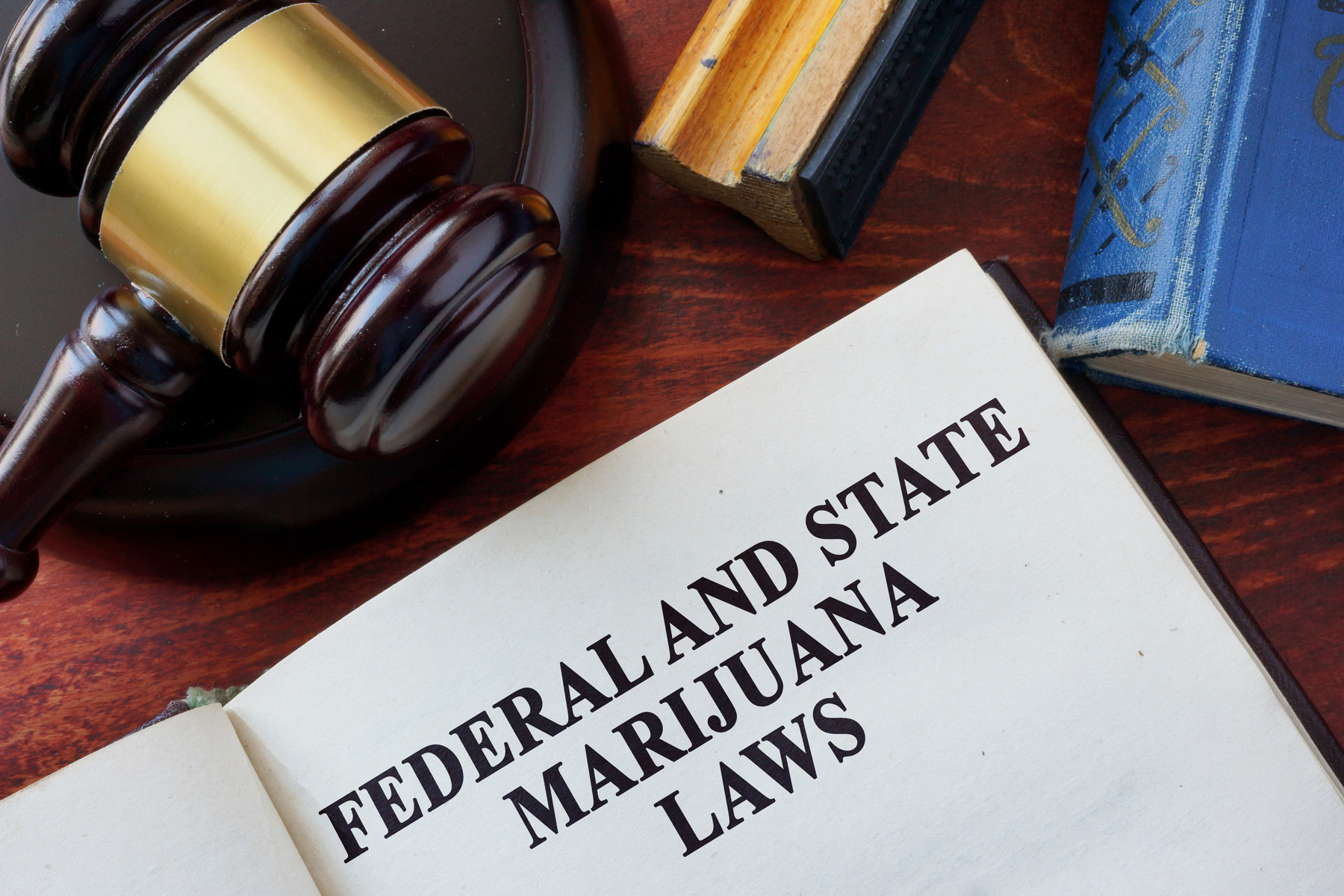 A book open to a page titled "Federal and State Marijuana Laws" sits on a desk beside a judge's gavel and references to Federal Legal Compliance for California M-License Operators. Ca NORML